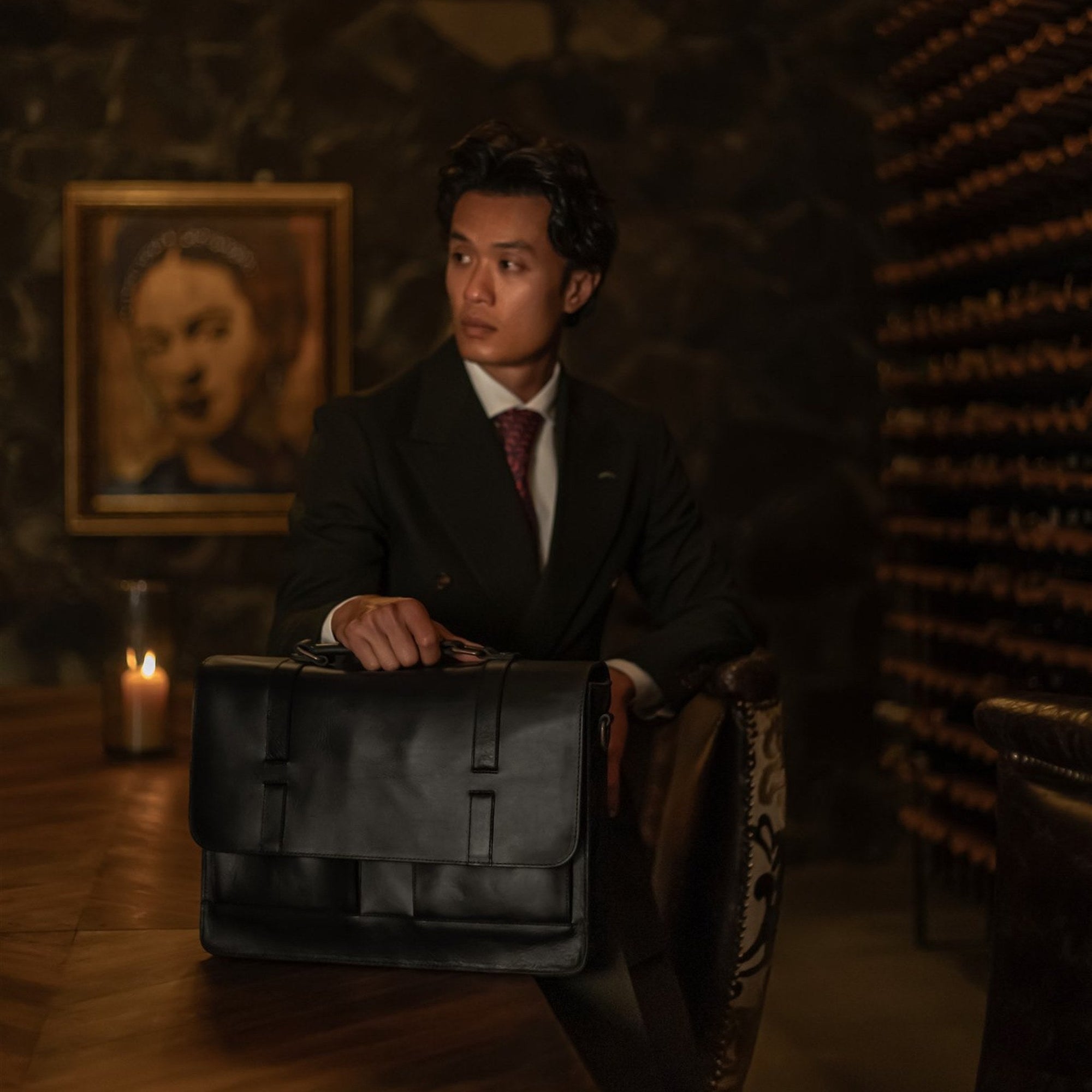 Man seated in a wine cellar with the Jefferson Leather Messenger Bag in Vintage Black.
