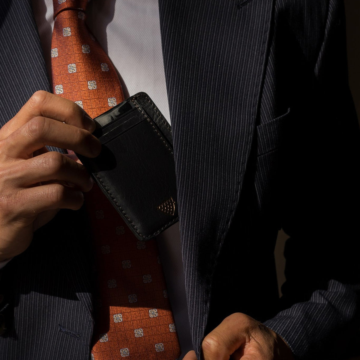 Man in a pinstripe suit and orange tie slipping the Jefferson Leather Slim ID Wallet in Vintage Black into his jacket.
