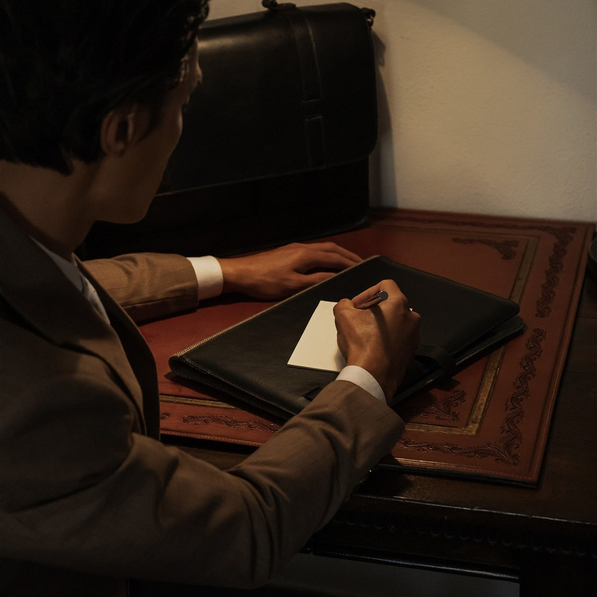 Man writing at a desk with the Jefferson Leather Travel Portfolio in Vintage Black.