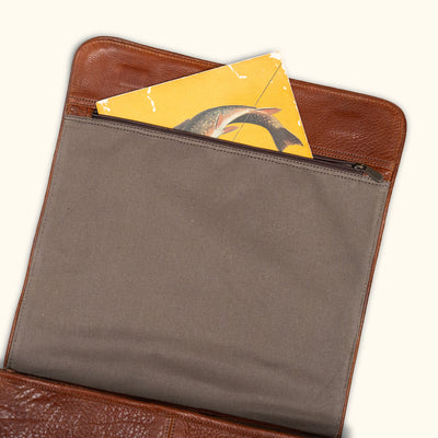 Close-up of an open brown leather laptop sleeve with a yellow vintage postcard partially visible, highlighting practical and stylish storage.