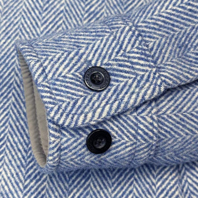 Close-up of a blue and white herringbone patterned fabric, showing a folded cuff with two black buttons.