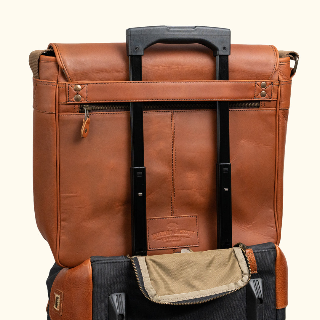 Elegant amber brown leather messenger bag featuring a spacious interior and secure flap closure. Perfect to hold on to luggage.