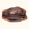 Detailed interior of a brown leather briefcase with storage for pens, cables, and a laptop.