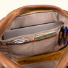 Open tan leather briefcase showcasing storage for a laptop, cable, and accessories.