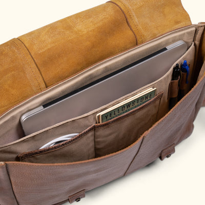 Interior of a leather messenger bag with pockets for a laptop, cable, and writing tools.