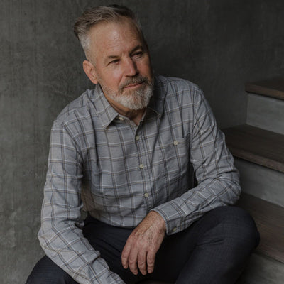 Man in the Windsor Cotton Shirt in Stone Pane, seated against a concrete wall