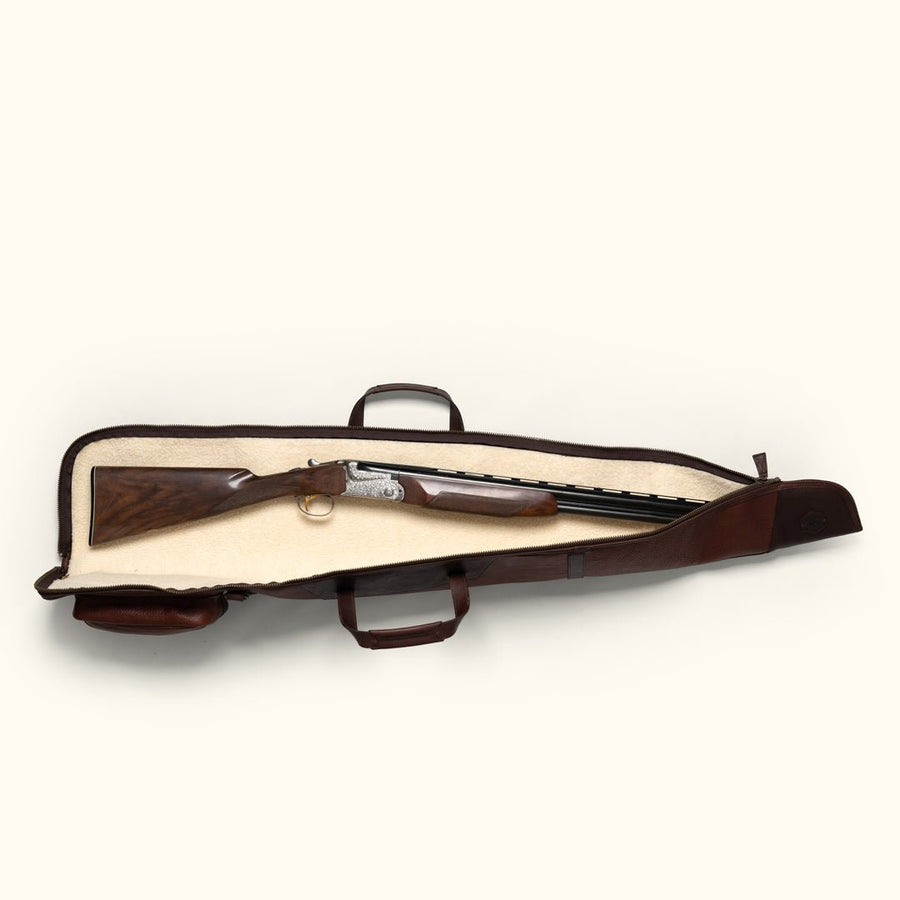 Open full grain leather shotgun case with a shotgun laid on the cream sherpa lining