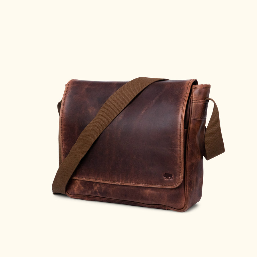 Elegant dark oak brown leather satchel with a wide, adjustable canvas strap, showcasing a smooth, well-worn patina and classic design.