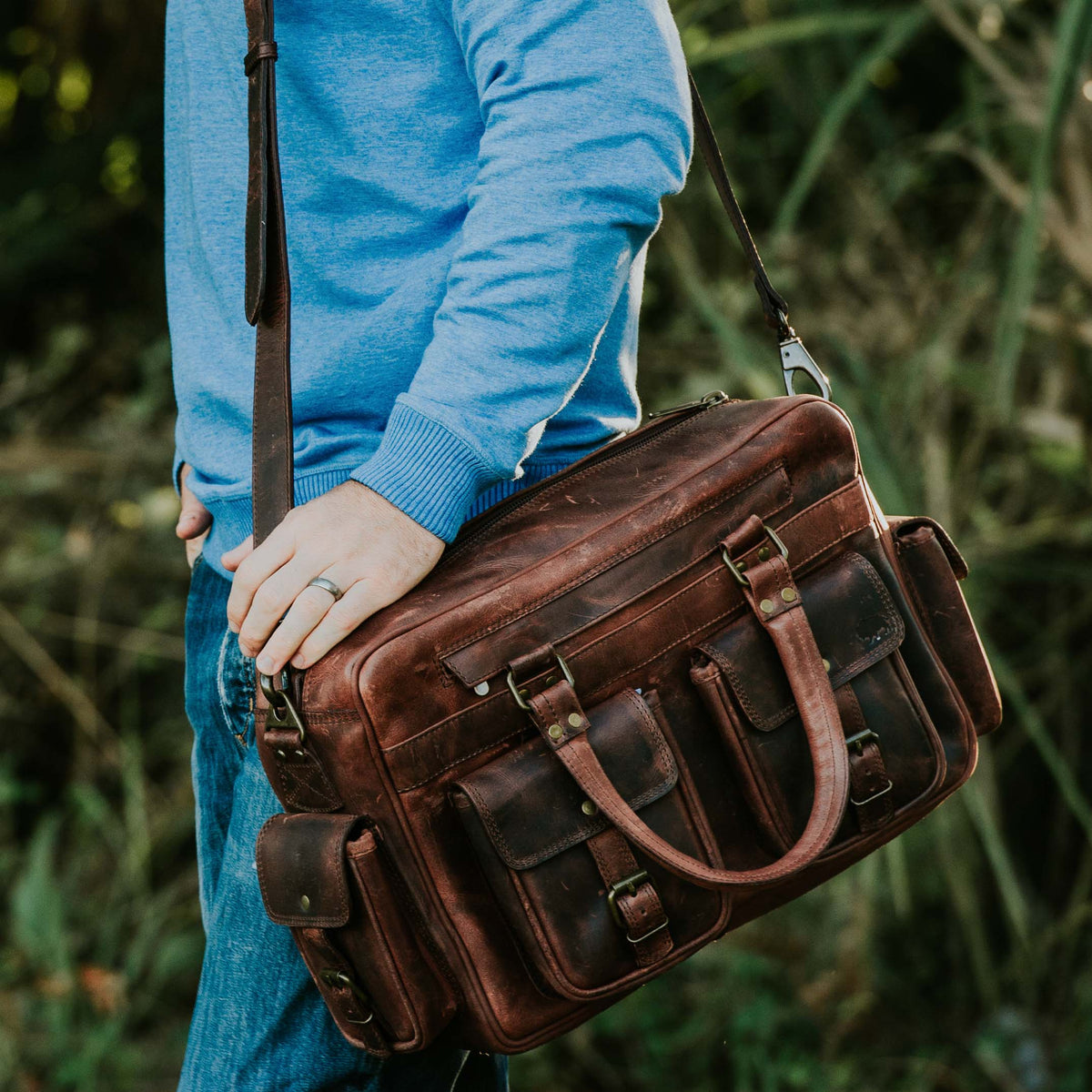  Rugged dark oak leather pilot bag displayed in an outdoor setting, featuring durable straps, buckle closures, and a spacious design, perfect for adventurous travel.
